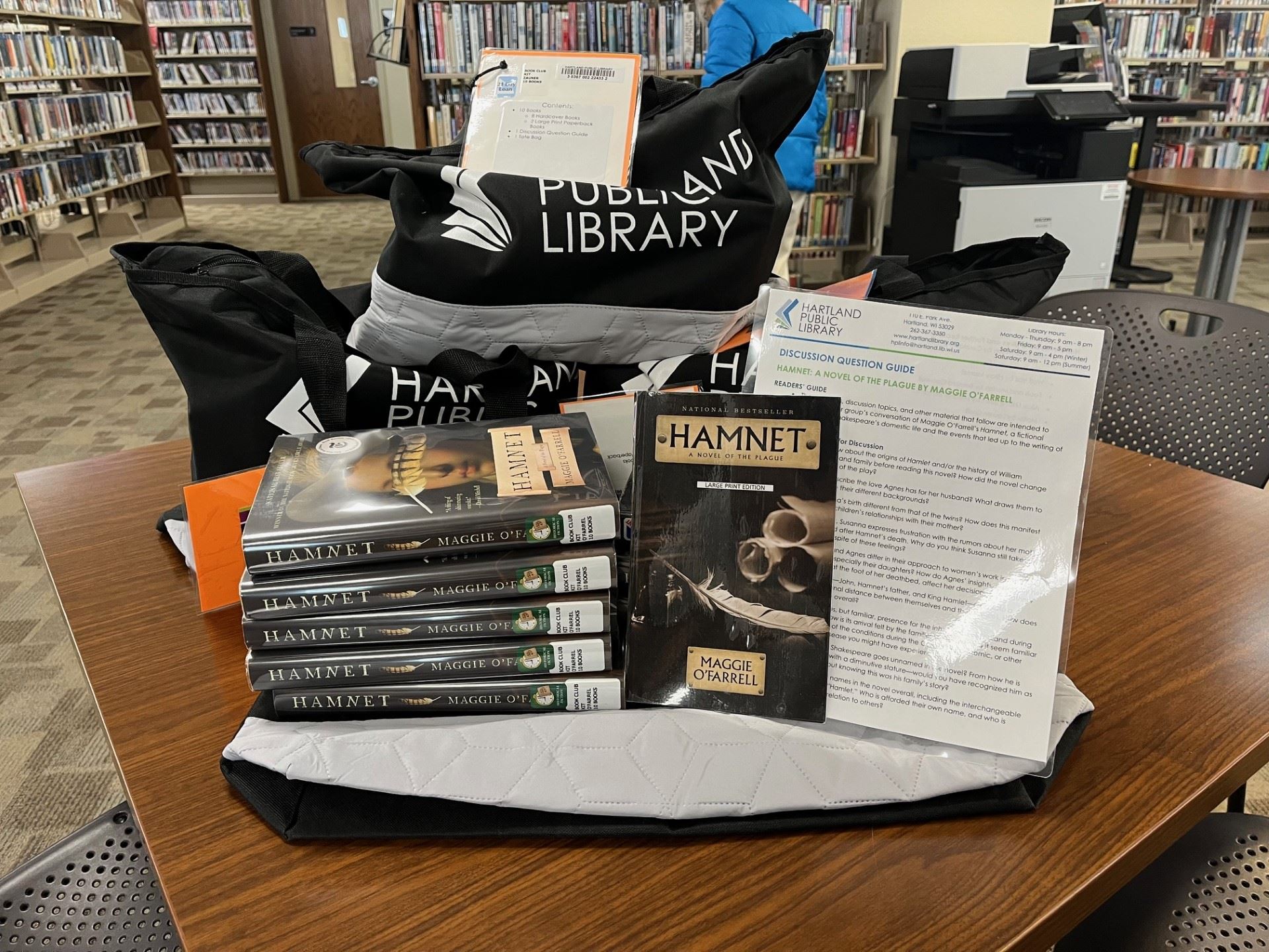 Three black bags stacked behind two stacks of books and a sheet of paper